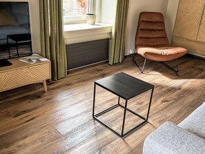 A modern living room with a wooden floor, a black metal table, a brown leather chair, a TV on a wooden stand, and a window with curtains. - Maloja Alpine Lodge by Interhome (Maloja)
