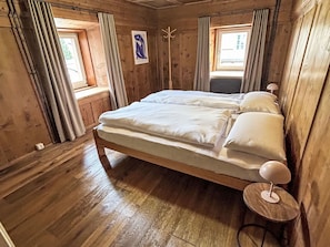 A wooden room with a bed, two windows, and a coat rack. - Maloja Alpine Lodge by Interhome (Maloja)