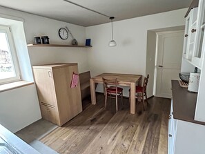 A compact kitchen with a wooden table and chairs, a refrigerator, a clock, and a window. - Maloja Alpine Lodge by Interhome (Maloja)