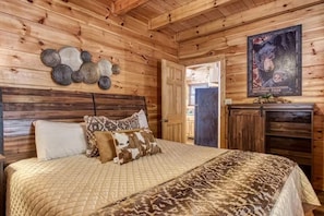 A wooden cabin bedroom with a bed, pillows, a wall-mounted clock, and a poster. - Sleeps 10, Game Room, Arcade, Hot Tub, Mountain Views, 6 Mi to Dollywood (Sevierville)