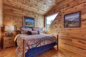 Une chambre dans une cabane en bois, avec un lit, des tables de chevet et deux tableaux encadrés accrochés aux murs.