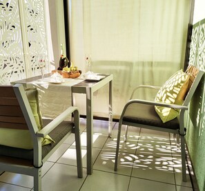 A dining area with a table set for two, a chair with a cushion, and a decorative wall with cut-out patterns. - Ascona Vacation Rental 200 meters from Lake Maggiore (Ascona)