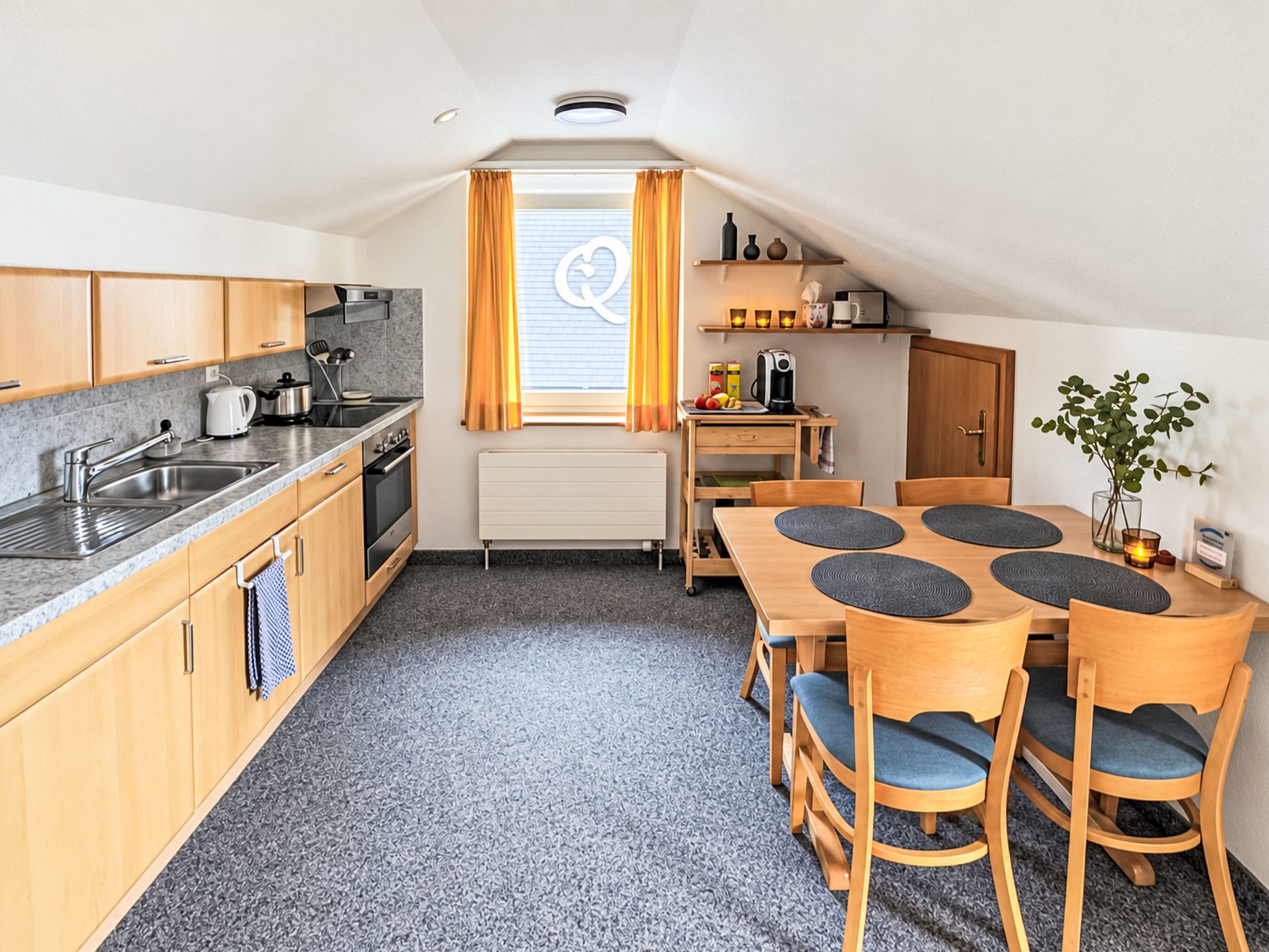 Cocina compacta con zona de comedor, que incluye una ventana con cortinas, un radiador y una pequeña mesa con sillas.