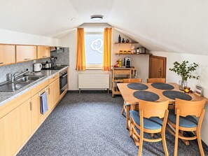 Cocina compacta con zona de comedor, que incluye una ventana con cortinas, un radiador y una pequeña mesa con sillas.