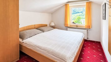 Habitación individual con una cama y cabecera de madera, una ventana con cortinas, un radiador y una alfombra roja.