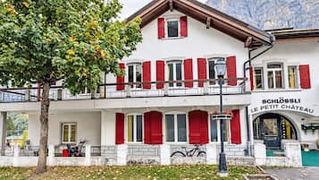 Un edificio de dos pisos con contraventanas rojas, un balcón y un letrero que dice 'SCHLOSSLI LE PETIT CHATEAU'.