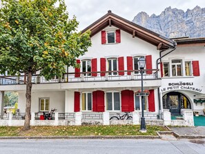 Un edificio de dos pisos con contraventanas rojas, un balcón y un letrero que dice 'SCHLOSSLI LE PETIT CHATEAU'.