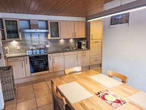A modern kitchen with wooden cabinets, a built-in oven, and a dining area with a wooden table and chairs. - La ferme du sommet de Pouillerel by Interhome (La Chaux-de-Fonds)