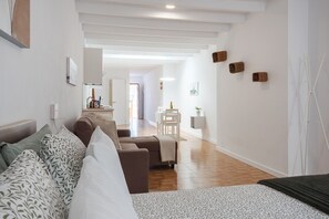 A modern hotel room with a sofa, a bed, a desk, and a chair. There is a hallway leading to a bathroom and a kitchen area. - Your Loft in the Heart of Lanzarote: Charm, Tranquility, and Volcanoes (TINAJO)