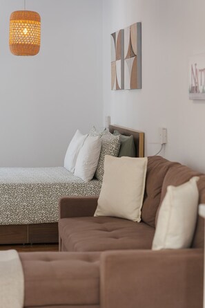 Ein Schlafzimmer mit einem Bett, einem braunen Sofa, einer Hängeleuchte und abstrakter Wandkunst.