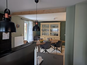 A kitchen with a dining area, wooden beams, a cabinet with glass doors, and a window with curtains. - Country House Nestled Among Lakes and Fields (Nordwestuckermark)