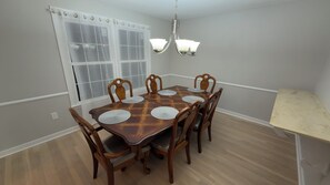 A dining room with a wooden table, six chairs, a chandelier, and a window with curtains. - Enjoyable 4-bedroom house with AC in charming Silver Spring, MD. (Silver Spring)