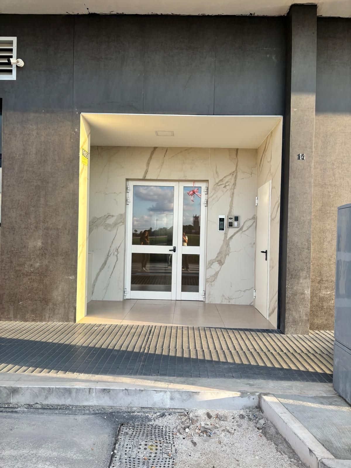 A modern building entrance with a glass door, a keypad, and a number '14' on the wall.