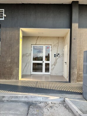 Entrada moderna de un edificio con puerta de cristal, un teclado numérico y el número 14 en la pared.