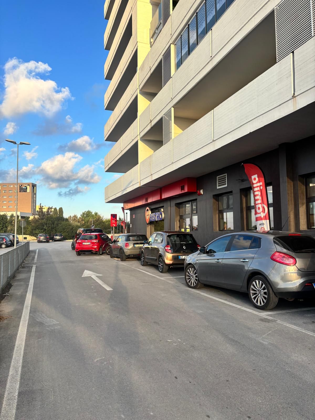 Un estacionamiento con autos estacionados frente a un edificio con toldo rojo y un cartel que dice 'BISTRO'.