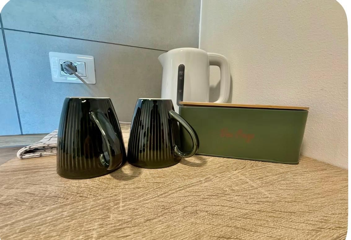 Una superficie de madera con dos tazas negras, una taza blanca y una caja verde con un logotipo.