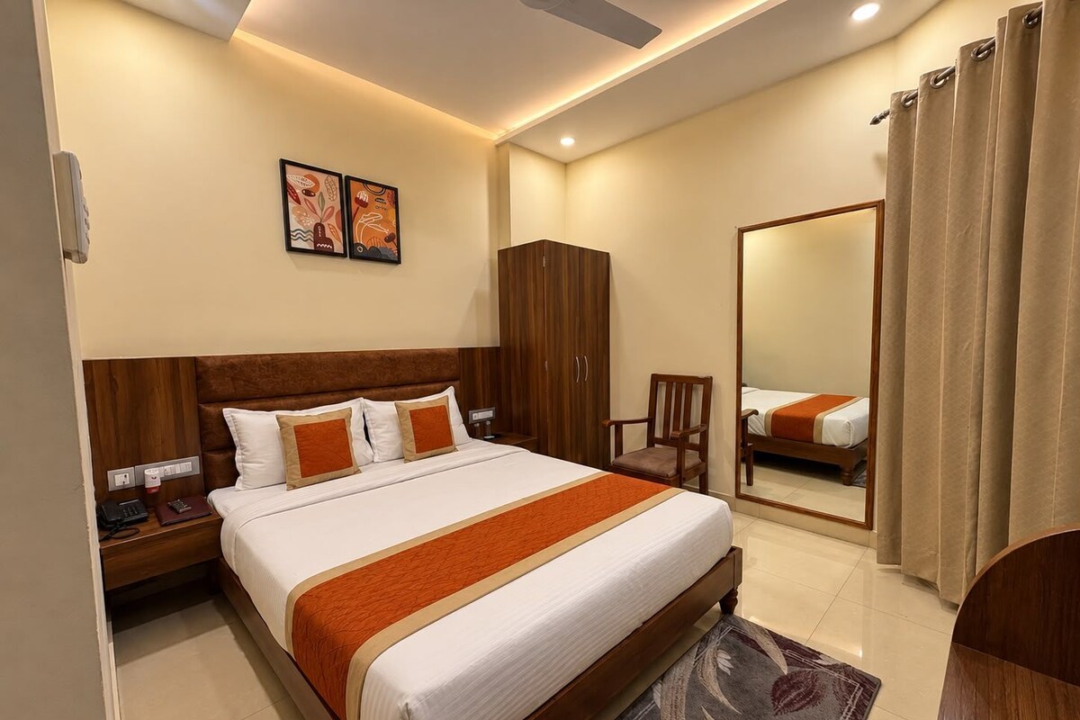 A hotel room with a large bed, a wooden headboard, a nightstand, a chair, a mirror, and a wardrobe.