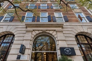 Fachada de edificio con múltiples ventanas, una entrada central arqueada y letreros para una cafetería y una tienda de delicatessen.