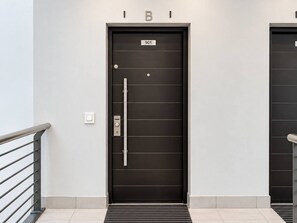 The Apartment 901 Entrance: A charcoal-black front door marked 901, featuring horizontal panel detailing, a long stainless steel handle and secure locking hardware, positioned along a tiled corridor with metal safety railings. - New prospect Mandela Rhodes apartment (Cape Town)