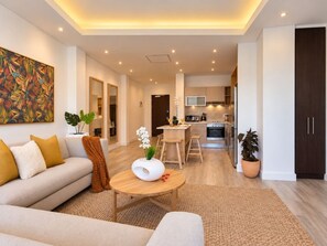A modern living room with a sofa, coffee table, and a kitchen in the background. - New prospect Mandela Rhodes apartment (Cape Town)