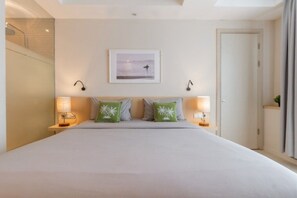 A hotel room with a large bed, two bedside lamps, a framed picture on the wall, and a door to the right. - Digital Nomad Studio Room Kuta (Badung)