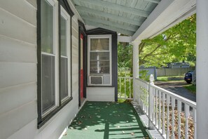 Eine überdachte Veranda mit einer grünen Matte, einem weißen Geländer und Blick auf eine Wohnstraße.