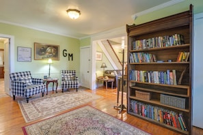 Uma sala de estar com poltronas estampadas, estante de livros, pintura e tapete.