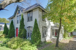 A two-story house with a red door, multiple windows, and a front porch. - Hike, Explore & Unwind: Finger Lakes B&B Suite (Interlaken)