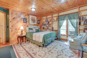 A cozy bedroom with a wooden ceiling, a bed with a green bedspread, a bedside table with a lamp, a bookshelf, and a window with curtains. - Hike, Explore & Unwind: Finger Lakes B&B Suite (Interlaken)