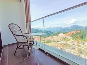 A balcony with a wicker chair and a small table, overlooking a construction site with mountains in the background.