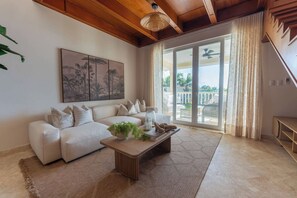 Una sala de estar con un sofá, una mesa de centro con objetos decorativos, un cuadro en la pared y vistas a través de puertas de vidrio.