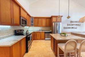 Una cocina con armarios de madera, electrodomésticos de acero inoxidable, encimera de granito y una zona de comedor con sillas de mimbre.