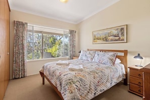 Ein Schlafzimmer mit großem Fenster, einem Bett mit Blumenmuster auf der Bettwäsche, einem Nachttisch und einem Gemälde an der Wand.