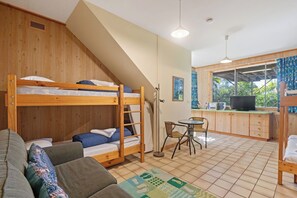 Ein Schlafsaalzimmer mit Etagenbetten, einer kleinen Küchenzeile, einem Esstisch und einem Fenster mit Blick auf Grünflächen.