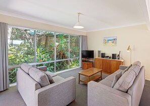 Ein Wohnzimmer mit großem Fenster, einem Fernseher, einem Holzschrank und einem Sofa.