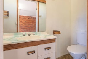 Ein Badezimmer mit einem weißen Waschbecken, einem Spiegel, einer Holzkommode und einer Toilette.