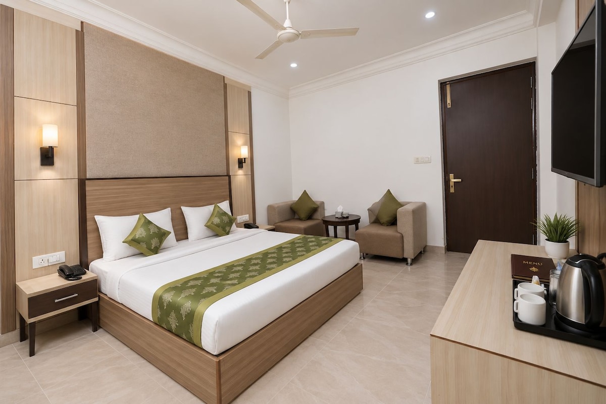 Habitación de hotel con cama, mesitas de noche, escritorio, silla, televisor y ventilador de techo.