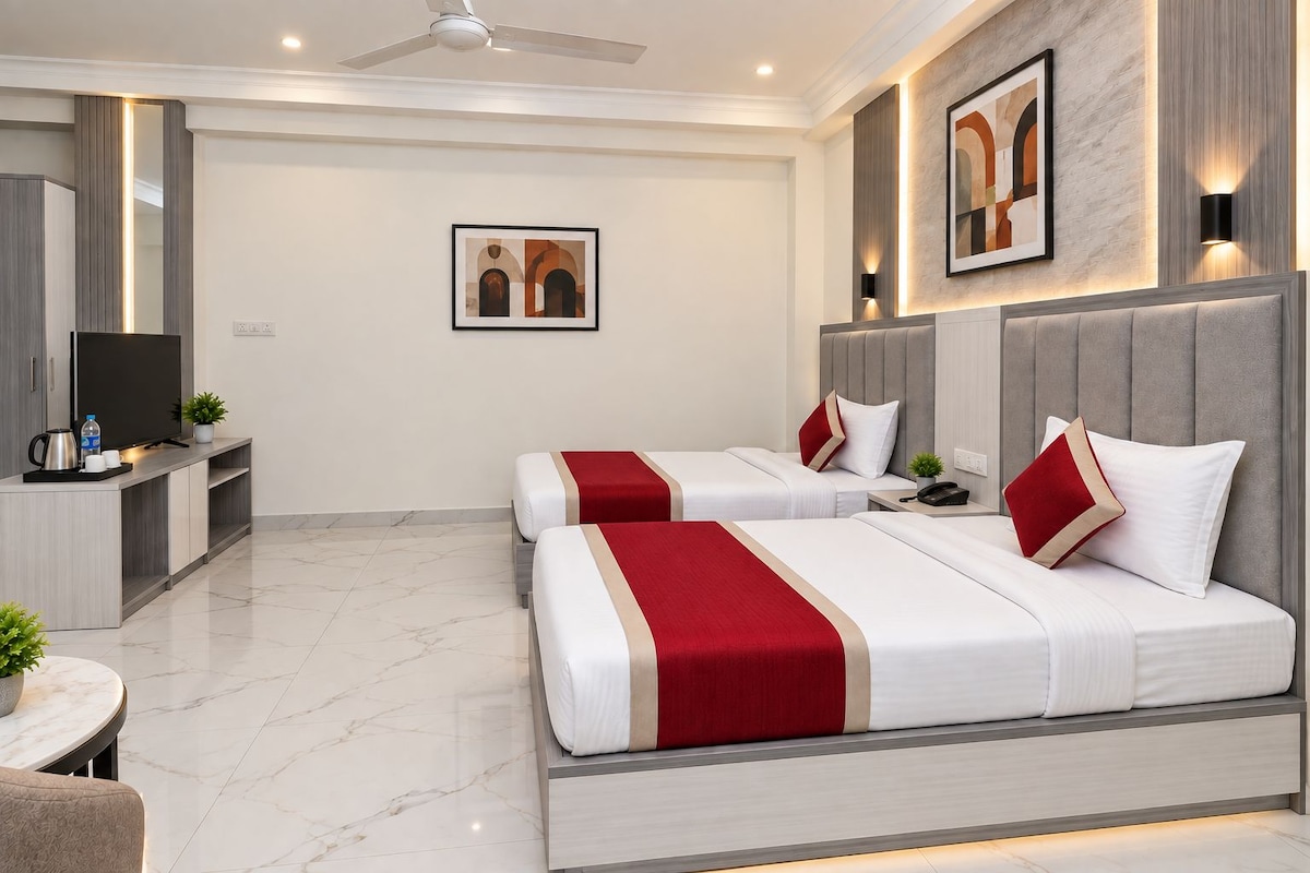 Habitación de hotel con dos camas, televisión, escritorio y ventilador de techo.