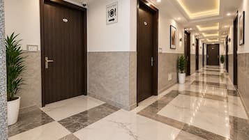 Un pasillo de hotel con suelo de mármol, puertas de madera y plantas en macetas.
