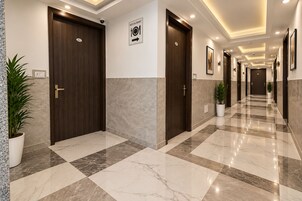 A hotel corridor with marble flooring, wooden doors, and potted plants.