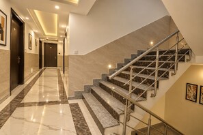 A modern hotel interior with a marble-floored hallway, a staircase with metal railings, and framed artwork on the walls. - Hotel Apple Crest Inn (New Delhi)
