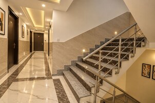 Un interior de hotel moderno con un pasillo de suelo de mármol, una escalera con barandillas metálicas y obras de arte enmarcadas en las paredes.