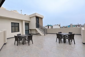 Una terraza en la azotea con dos mesas y sillas, una escalera y vistas de la ciudad.