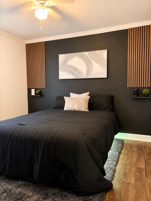 A modern bedroom with a large bed, a ceiling fan, and a wall-mounted abstract painting.