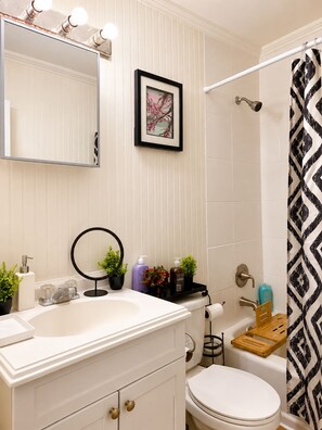A bathroom with a white sink, a mirror, a framed picture, a shower curtain, and a toilet.