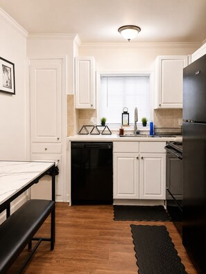 A kitchen with white cabinetry, a black refrigerator, a dishwasher, and a wooden floor.