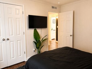 Ein Schlafzimmer mit einem Bett, einem an der Wand befestigten Fernseher und einer Pflanze.