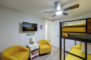 Habitació amb literes, televisió, ventilador de sostre i una taula petita amb una làmpada.