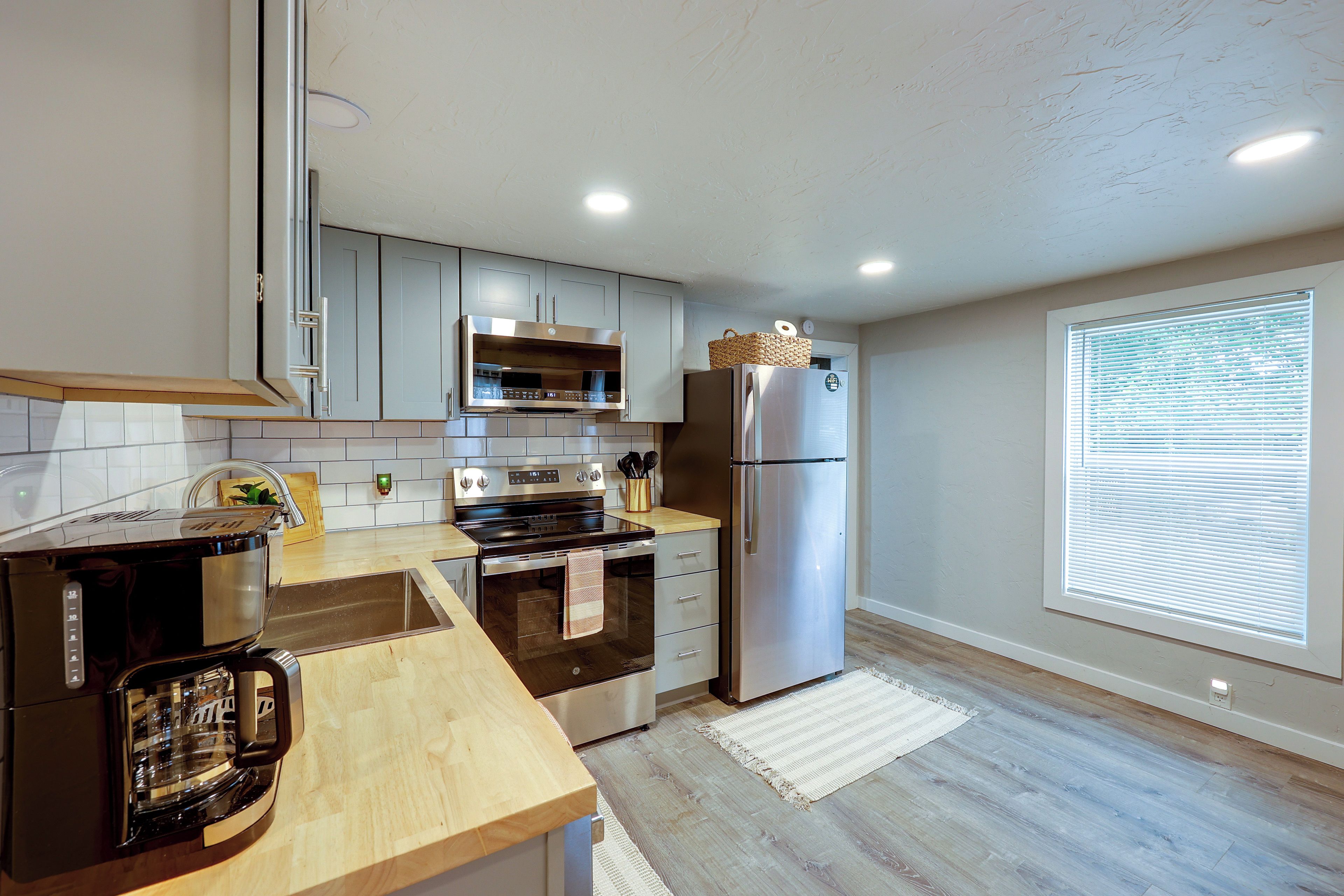 A modern kitchen with stainless steel appliances, wooden countertops, and a large window with blinds.
