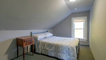 Une chambre avec un lit simple, une table de chevet, une fenêtre et un luminaire au plafond.